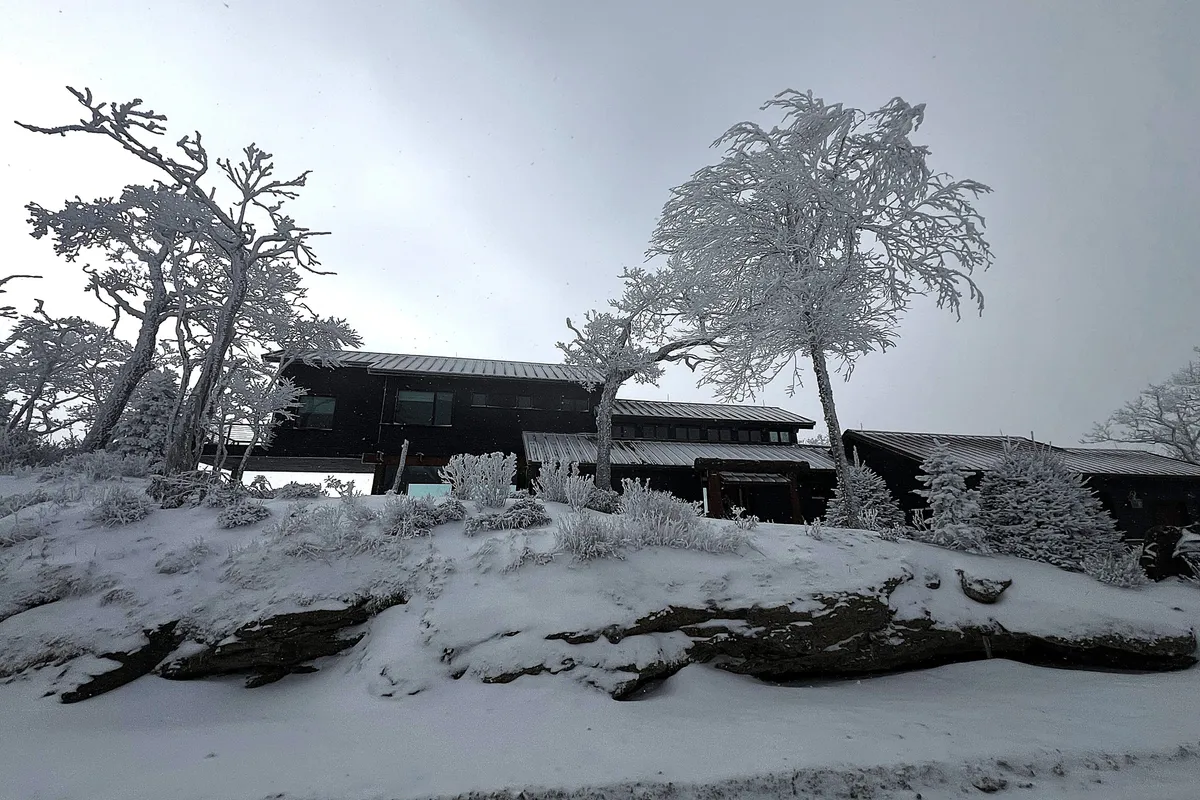 A snow-covered house surrounded by frosted trees and a rocky winter landscape. The scene highlights the property’s year-round appeal, specifically in winter, and the adventure opportunities that come with snowy weather.