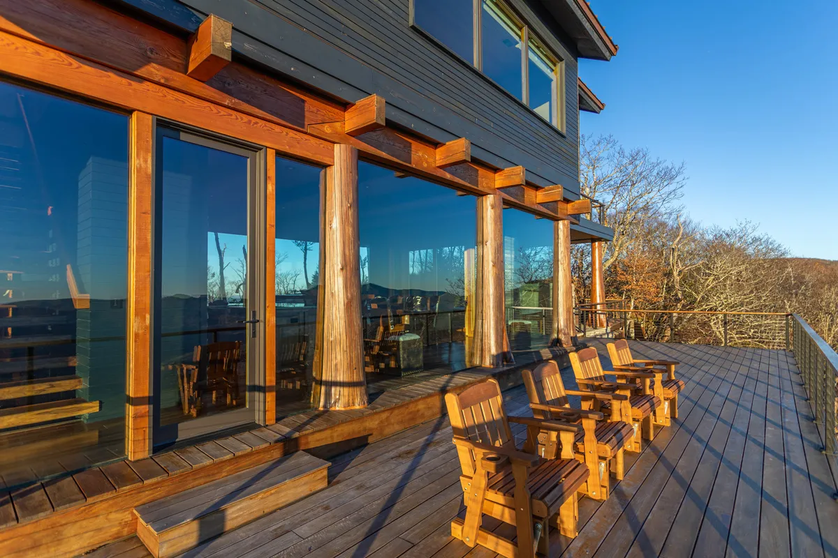 The image features the home’s deck with ample seating, large glass windows, and wooden columns, set against a backdrop of serene natural scenery. The space is clearly used for outdoor socializing, stargazing, and sunset watching, inviting exploration and connection to nature.