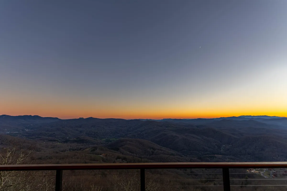 A breathtaking view of the mountain landscape at sunset, with vibrant colors spreading across the sky. The scene is tranquil and inspiring, evoking the allure of winery vistas, stargazing, and serene moments that define the area’s appeal.