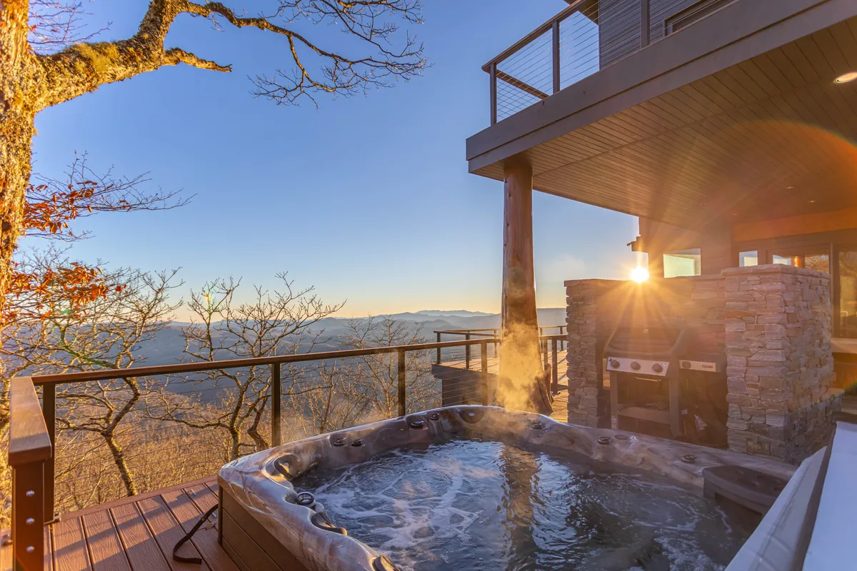A luxurious hot tub sits on a deck, offering clear views of the surrounding mountains and a glowing sunset. The inviting water, combined with the natural backdrop, evokes relaxation and rejuvenation, whether after a day of adventure or as a winter retreat.