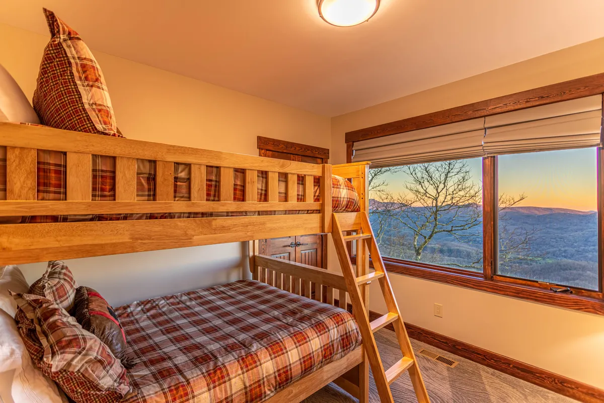A cheerful bunk room outfitted with full-over-full bunk beds dressed in plaid bedding, complemented by a large window bringing in natural light and mountain views. The room feels playful yet inviting.