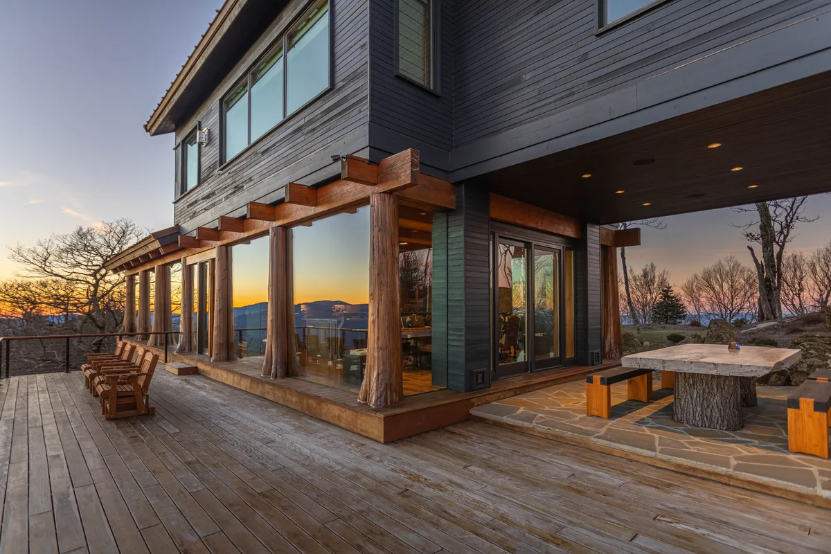 An exterior view of a large deck with ample dining space, wooden furniture, and sunset views. The scene is ready for al fresco meals, group gatherings, or quiet reflection, with mountain vistas providing a dramatic backdrop.